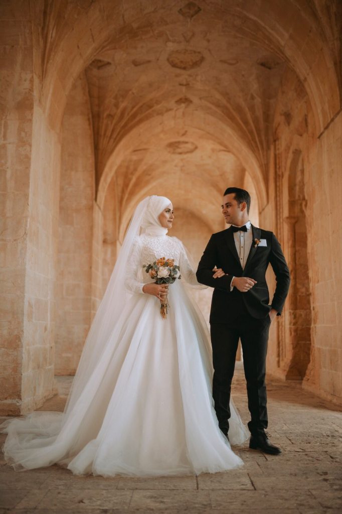 Elegant bride and groom in formal wedding attire posing in a historic stone corridor, captured by Al Ameen Wedding Planner Kochi.