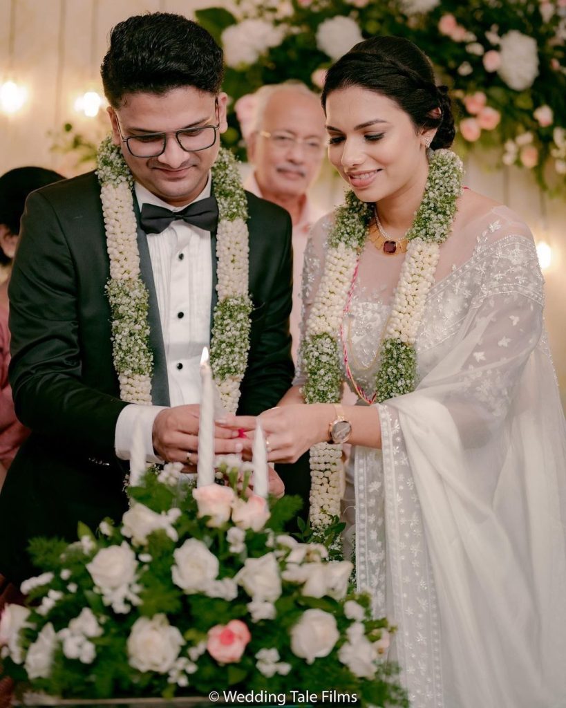 Bride and groom lighting ceremonial candles during an elegant Indian wedding, surrounded by floral arrangements and hanging lights — captured by Al Ameen Wedding Planner, Kochi.