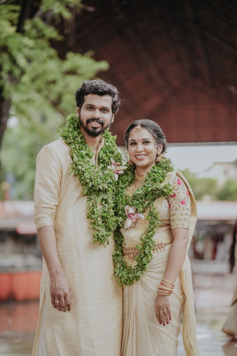 Traditional Kerala wedding couple in cream attire with green garlands, captured during outdoor ceremony by Al Ameen Wedding Planner Kochi.